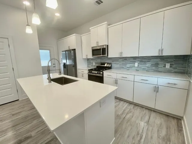 a kitchen with stainless steel appliances a stove top oven a sink a refrigerator white cabinets and wooden floor