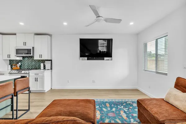 a living room with stainless steel appliances furniture a flat screen tv and a window