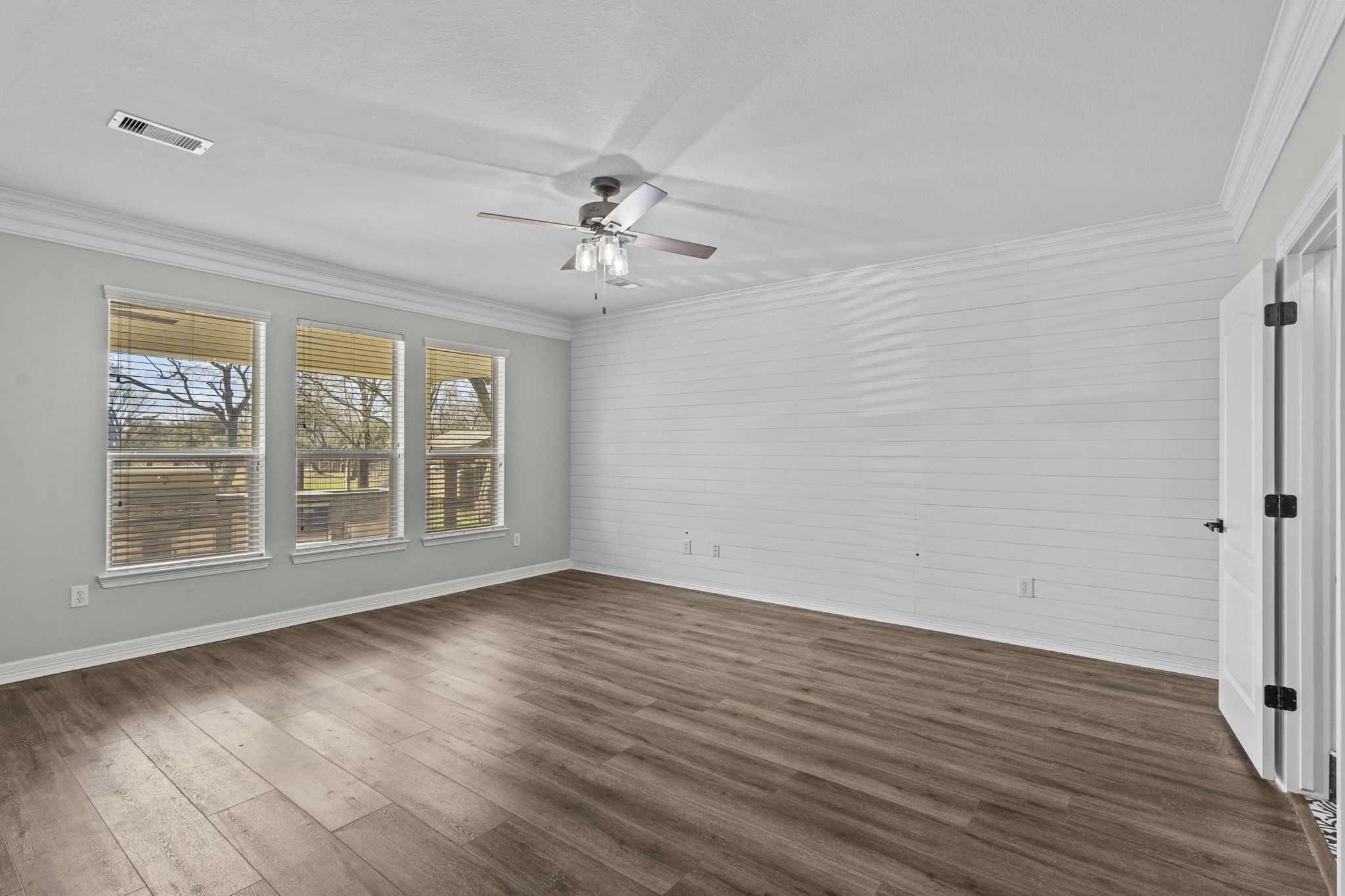 2730 Lawrence Road Kemah, TX 77565 - Photo 23 of 46 This spacious room features elegant wood flooring, a ceiling fan, and abundant natural light from three large windows. The shiplap accent wall and neutral paint provide a modern, cozy atmosphere.