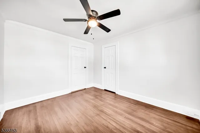 an empty room with wooden floor ceiling fan and windows