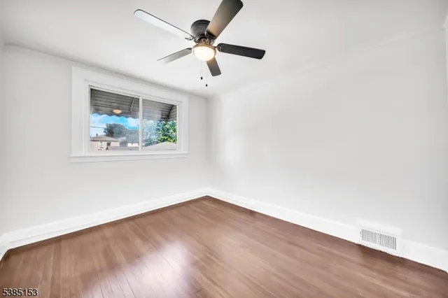 an empty room with wooden floor ceiling fan and windows