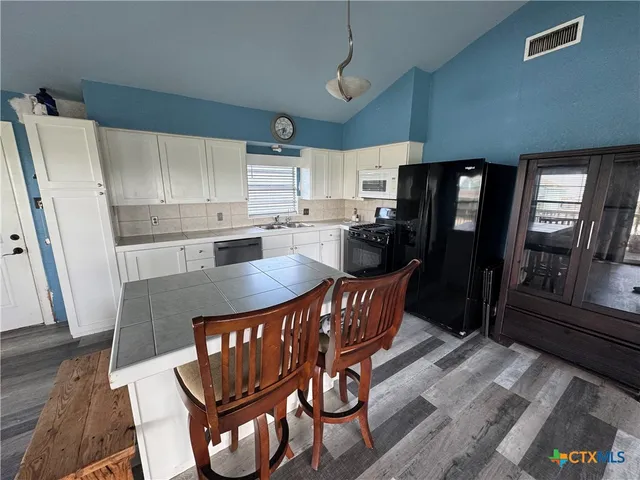 a kitchen with stainless steel appliances a dining table chairs refrigerator and sink