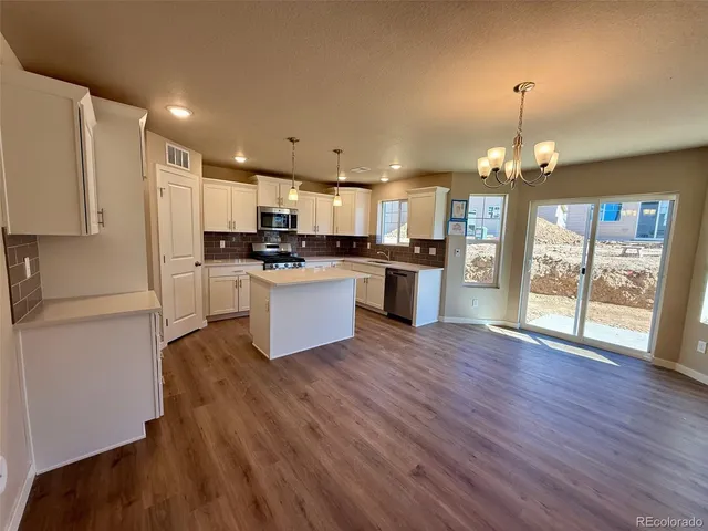 a kitchen with stainless steel appliances granite countertop a refrigerator a stove top oven a sink dishwasher and white cabinets with wooden floor