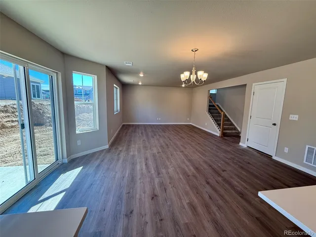 an empty room with wooden floor kitchen view and windows