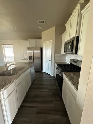 a large kitchen with a stove top oven a sink a refrigerator and white cabinets