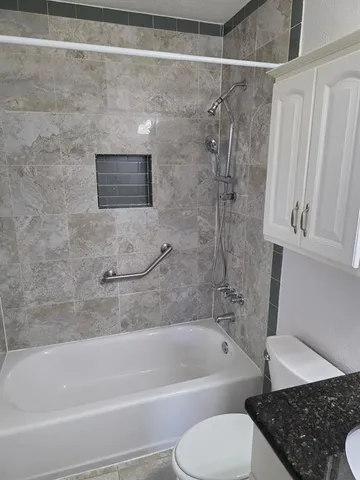 a bathroom with a granite countertop bathtub shower and toilet