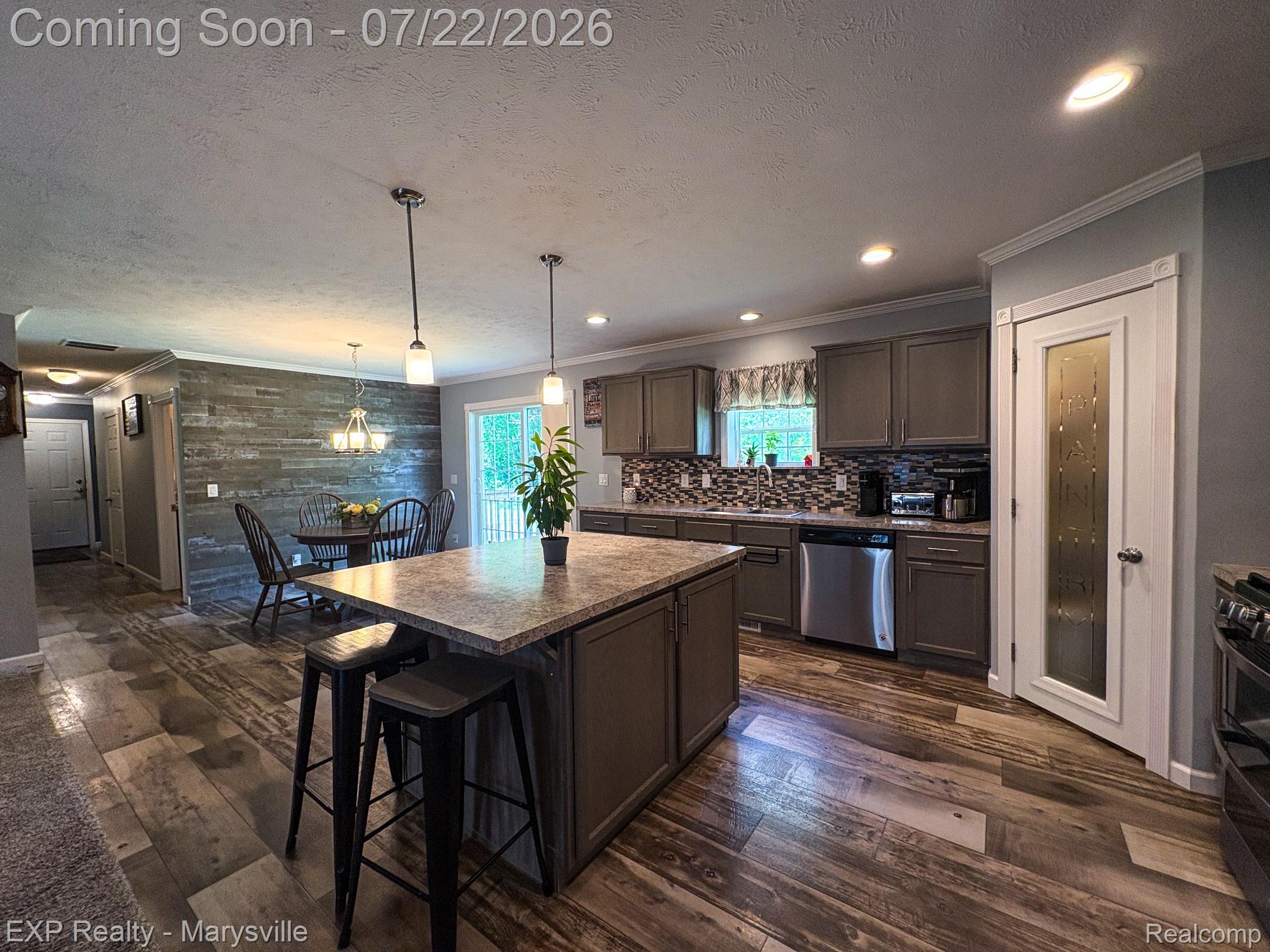 2601 Beach Road Port Huron, MI 48060 - Photo 19 of 34 Spacious kitchen and dining area featuring a central island, wood-finish flooring, stainless steel appliances, a mosaic tile backsplash, and a pantry with a frosted glass door