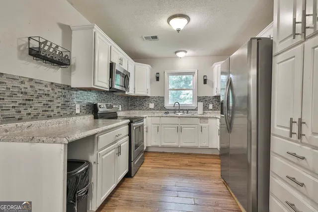 a kitchen with stainless steel appliances granite countertop a refrigerator a sink dishwasher a stove and white countertops with wooden floor