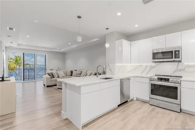 a kitchen with stainless steel appliances granite countertop a stove top oven a sink dishwasher a refrigerator and white cabinets with wooden floor