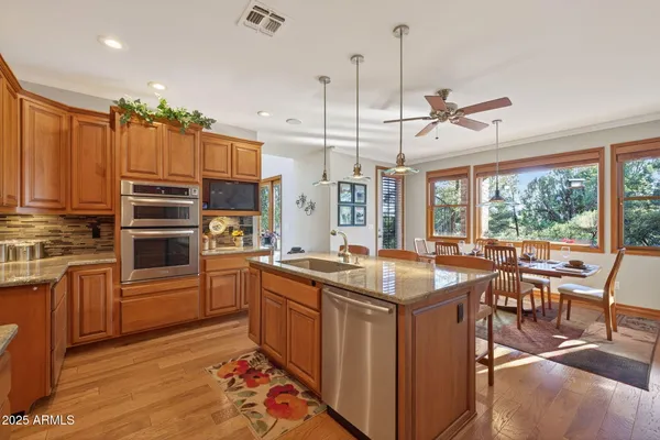 a kitchen with stainless steel appliances granite countertop a stove top oven a sink dishwasher a dining table and chairs with wooden floor