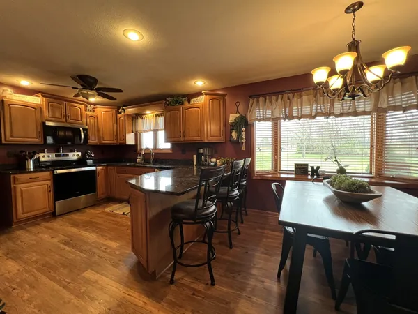 a kitchen with stainless steel appliances granite countertop a stove a sink a microwave a dining table and chairs with wooden floor