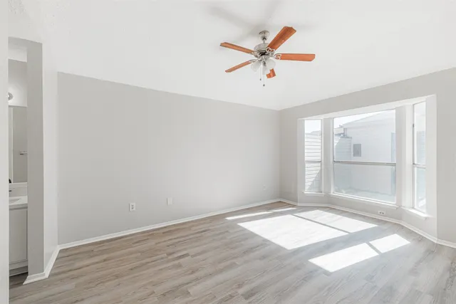 an empty room with wooden floor fan and windows