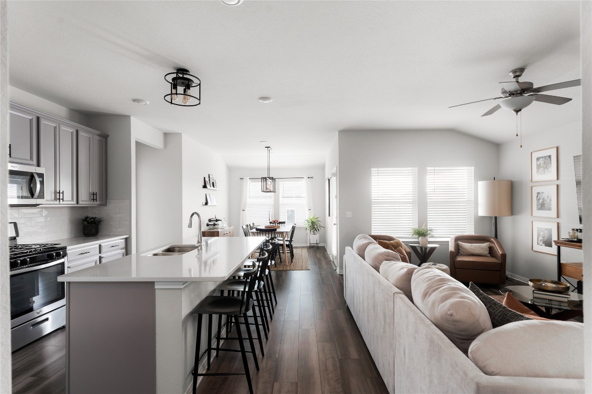 Living room featuring dark wood-style flooring, ceiling fan, and vaulted ceiling