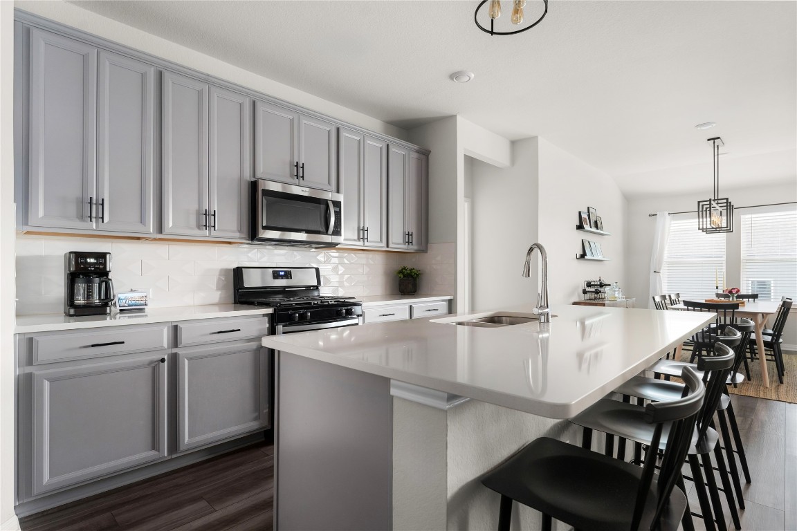 6511 Rounded Pebble Lane Buda, TX 78610 - Photo 3 of 25 Kitchen with decorative light fixtures, stainless steel appliances, gray cabinets, a kitchen island with sink, and tasteful backsplash