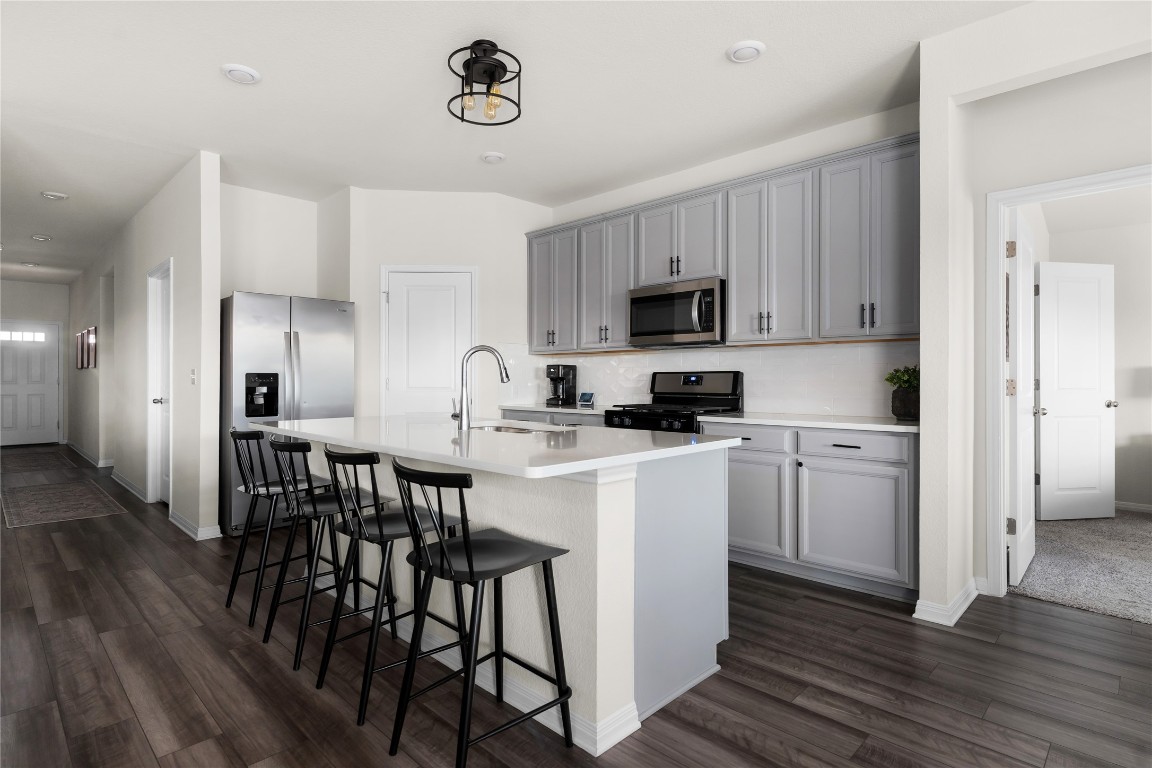6511 Rounded Pebble Lane Buda, TX 78610 - Photo 4 of 25 Kitchen featuring a kitchen breakfast bar, dark wood-style floors, gray cabinets, appliances with stainless steel finishes, and a kitchen island with sink