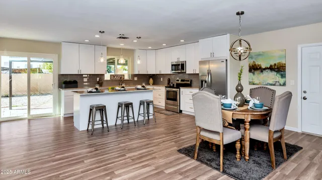 a dining area with stainless steel appliances kitchen island granite countertop a dining table chairs and a refrigerator