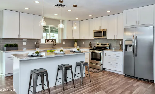 a kitchen with stainless steel appliances granite countertop a refrigerator a sink dishwasher a stove and white cabinets with wooden floor