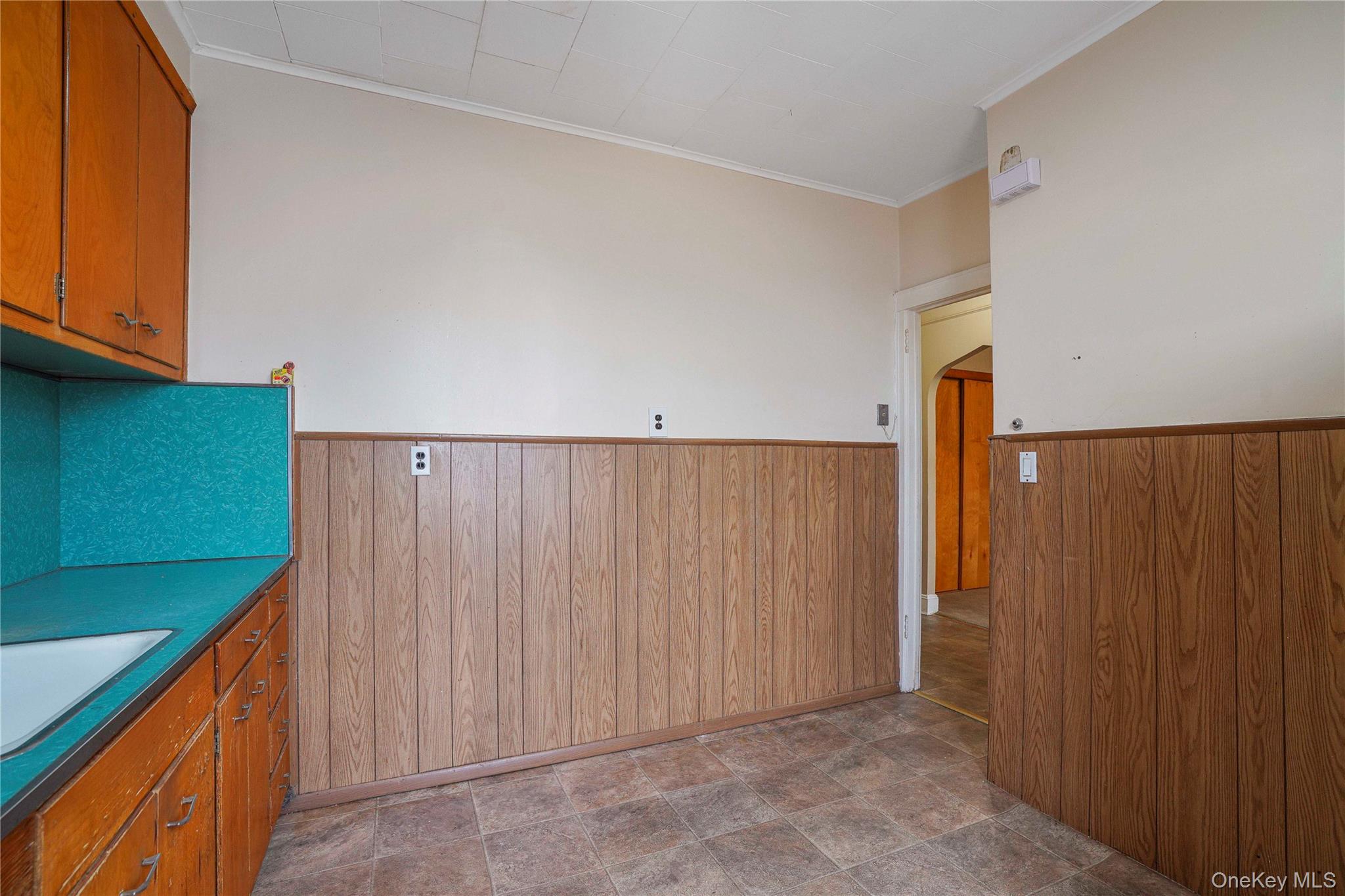 72-07 73rd Street Queens, NY 11385 - Photo 11 of 44 Kitchen featuring wood walls, brown cabinetry, crown molding, a wainscoted wall, and dark countertops