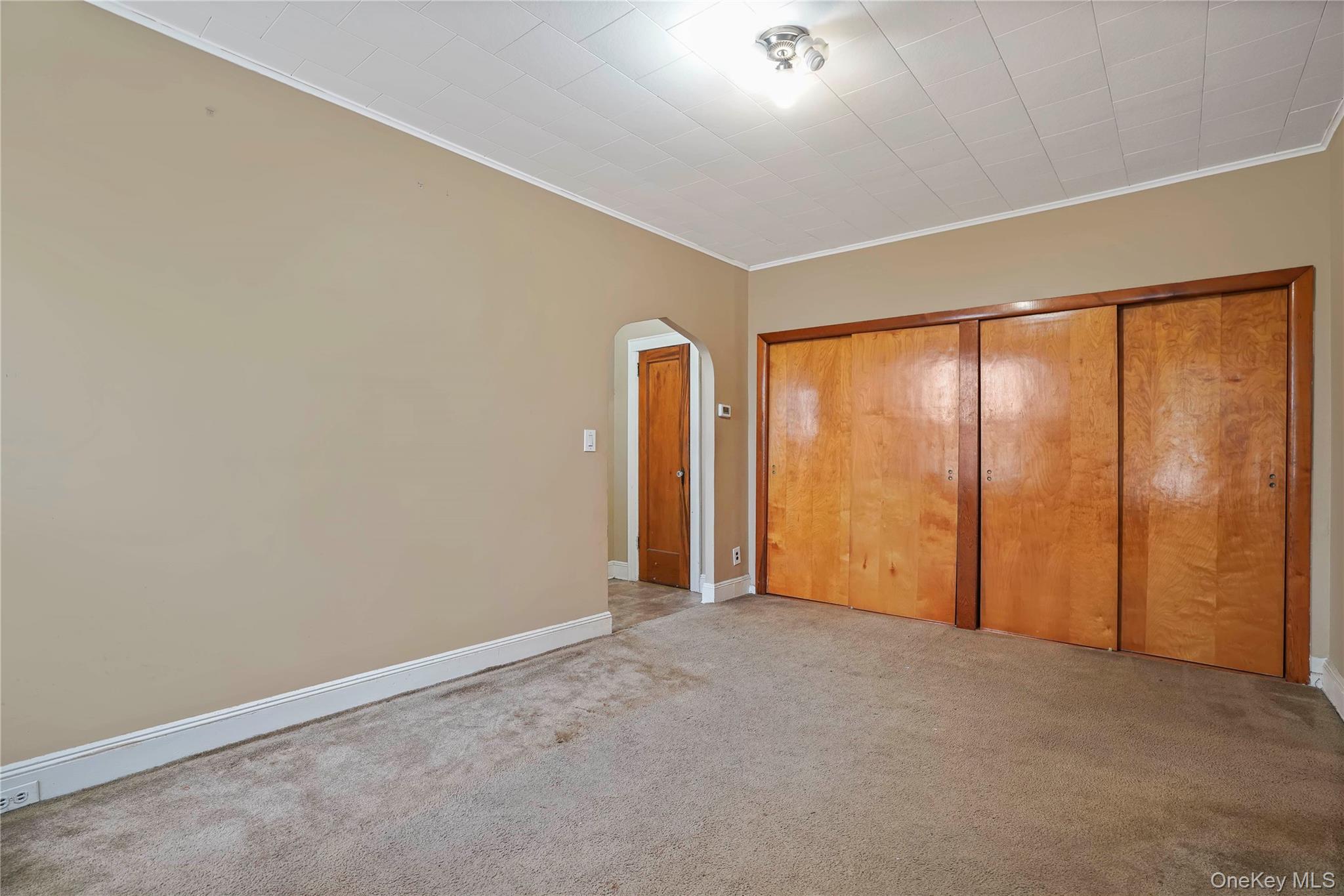 72-07 73rd Street Queens, NY 11385 - Photo 18 of 44 Unfurnished bedroom featuring arched walkways, a closet, crown molding, and light carpet