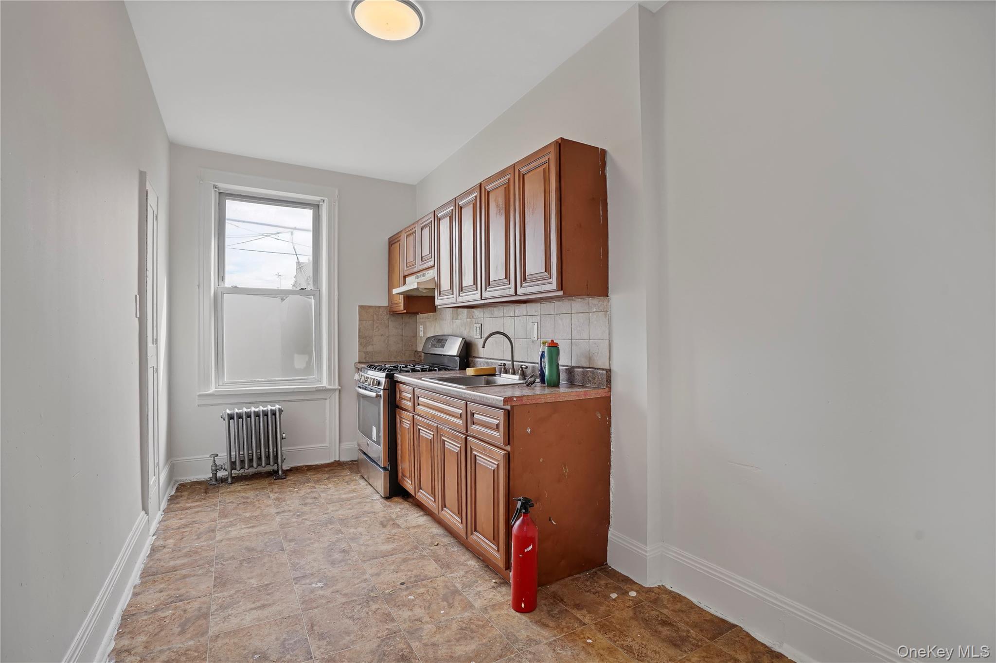72-07 73rd Street Queens, NY 11385 - Photo 24 of 44 Kitchen with brown cabinets, stainless steel gas range oven, tasteful backsplash, radiator heating unit, and stone finish floors