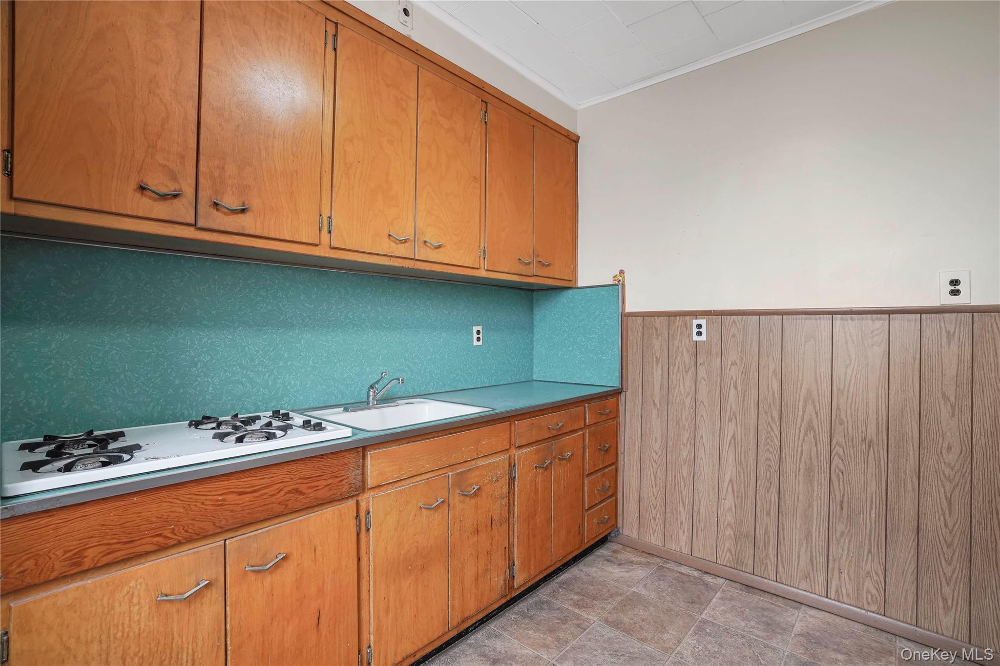 72-07 73rd Street Queens, NY 11385 - Photo 10 of 44 Kitchen with wooden walls, crown molding, brown cabinets, white gas stovetop, and wainscoting