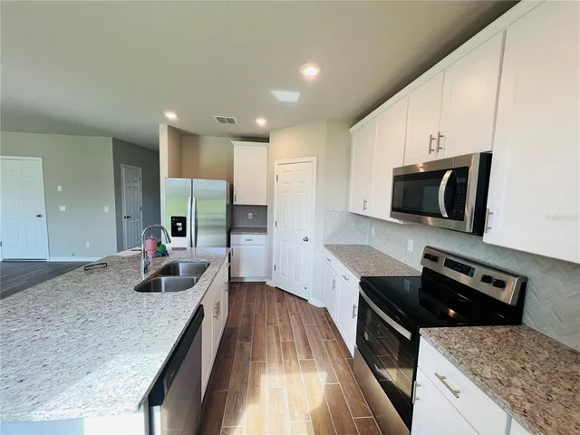 a kitchen with granite countertop stainless steel appliances a sink a stove top oven a counter space and cabinets