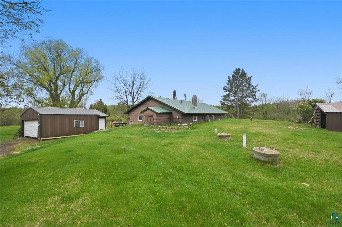 5190 County Road M Gordon, WI 54838 - Photo 6 of 31 Expansive green lawn surrounds a wood-sided house with a dark green roof, a separate garage with white doors, and an additional wood-sided outbuilding