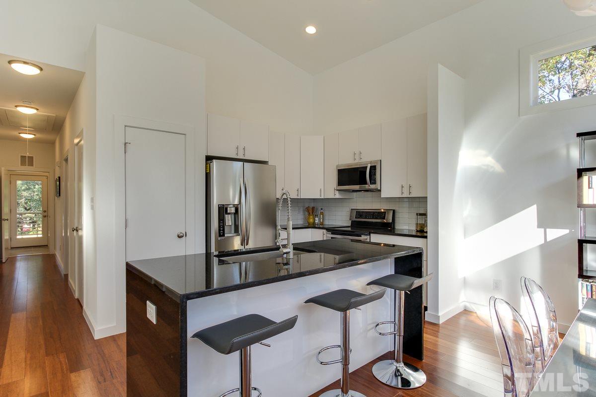 1306 South East Street Raleigh, NC 27601 - Photo 8 of 24 a kitchen with stainless steel appliances granite countertop a stove top oven a sink dishwasher a refrigerator and white cabinets with wooden floor