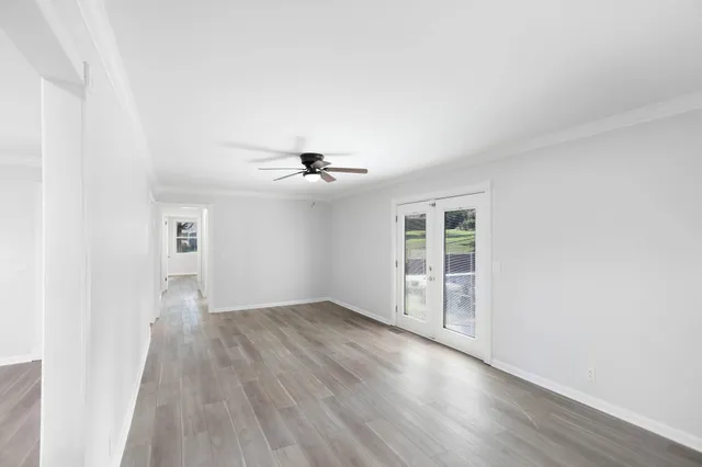 an empty room with wooden floor chandelier fan and windows