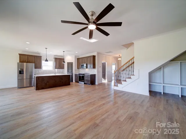 a view of a livingroom with a kitchen island wooden floor and a ceiling fan