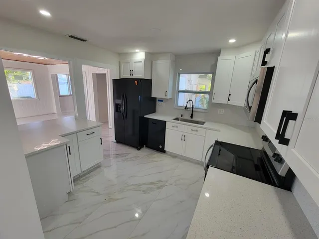 a large white kitchen with a sink a refrigerator and cabinets