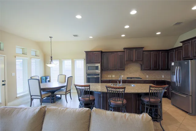 a kitchen with stainless steel appliances a dining table chairs refrigerator and cabinets
