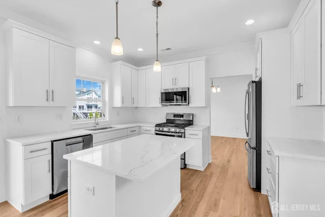 a kitchen with stainless steel appliances a stove a sink a refrigerator white cabinets and wooden floor