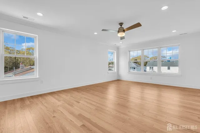 an empty room with wooden floor ceiling fan and windows