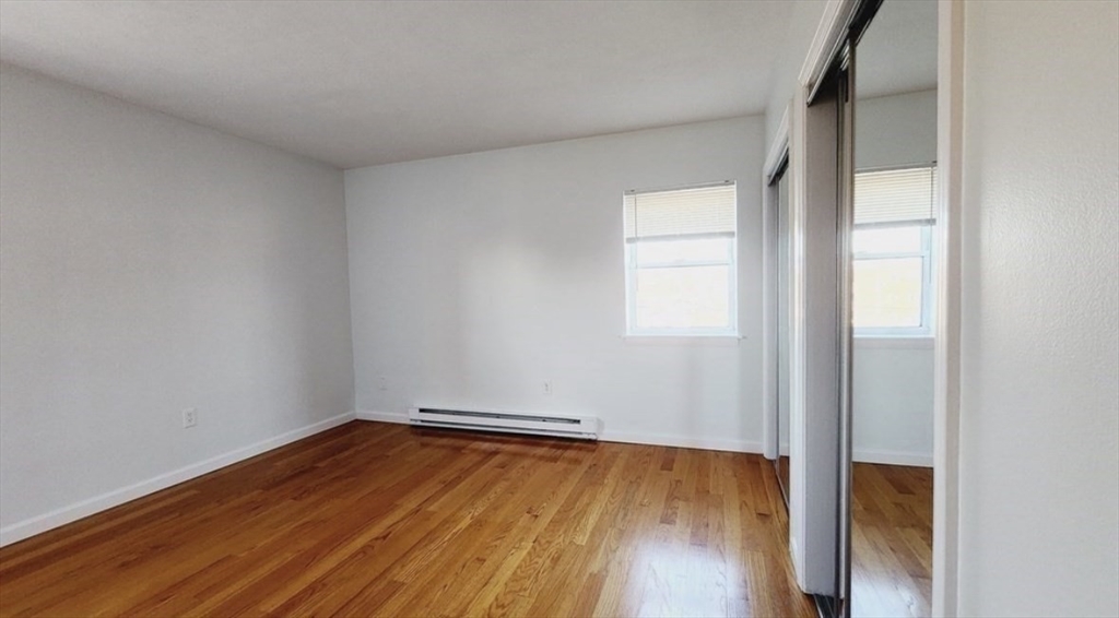 116 Spring Street, Unit D2 Boston, MA 02132 - Photo 5 of 9 an empty room with wooden floor and windows