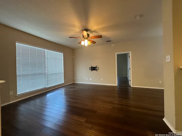 a view of an empty room with wooden floor and a ceiling fan