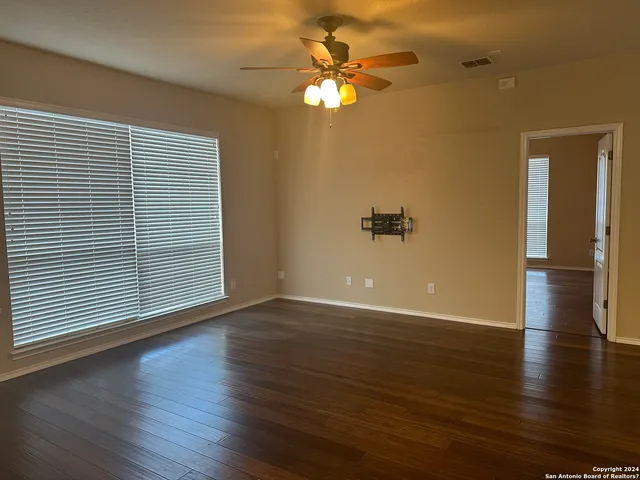 an empty room with wooden floor chandelier fan and windows