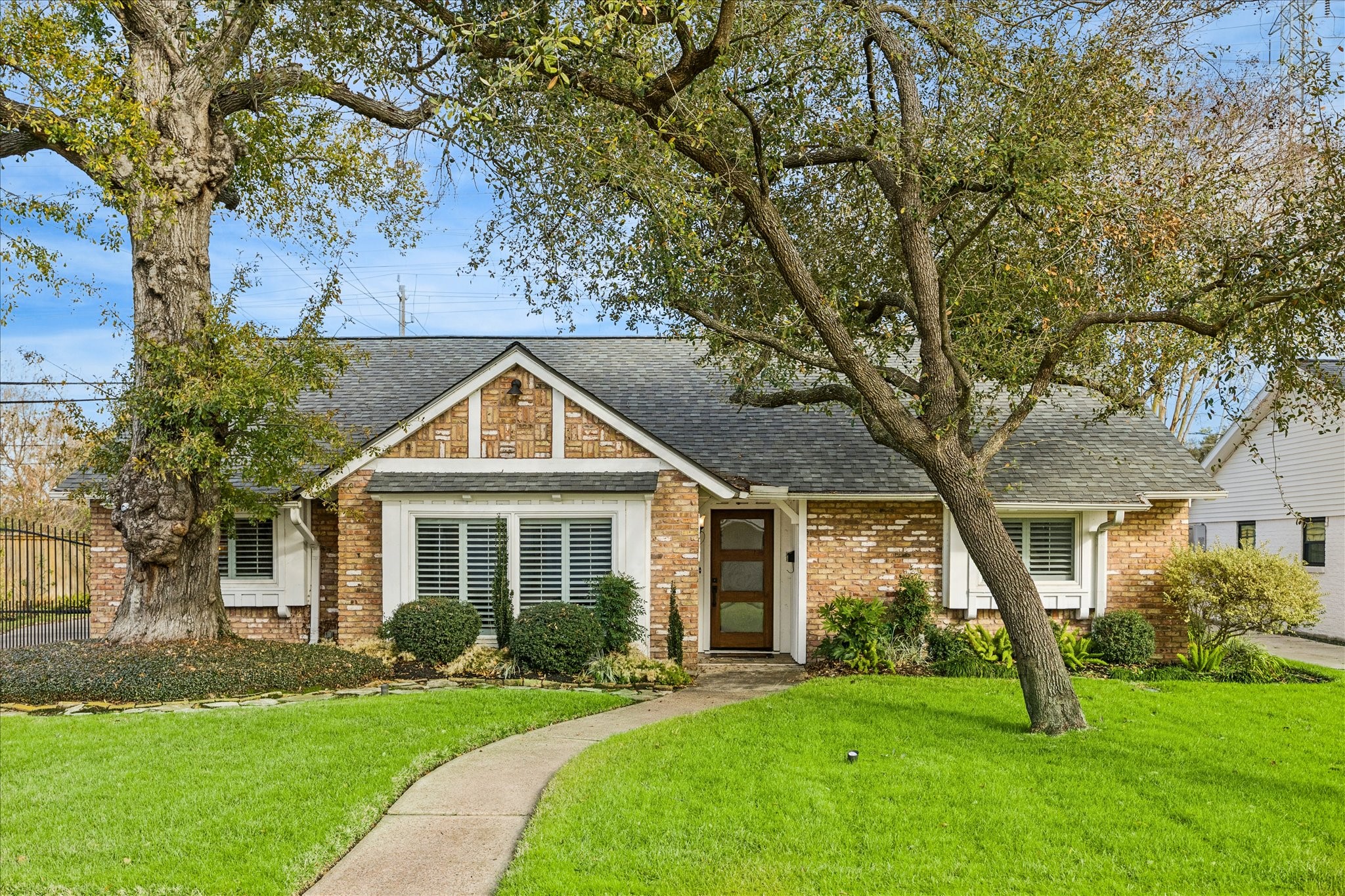 Charming brick home on an oversized corner lot, with a welcoming front yard, mature trees, and lush greenery. A curved pathway leads to the entrance, creating inviting curb appeal.