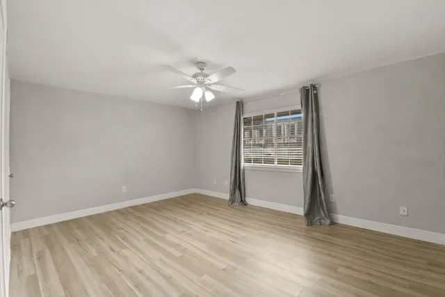 an empty room with wooden floor fan and windows
