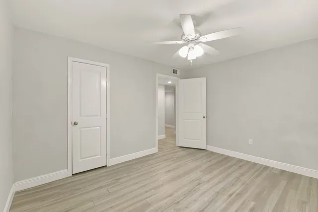 an empty room with wooden floor fan and windows