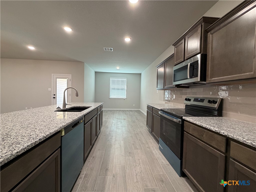 3008 Seeker Street Killeen, TX 76549 - Photo 7 of 25 a large kitchen with stainless steel appliances granite countertop a sink a stove top oven a refrigerator with wooden cabinets and floor