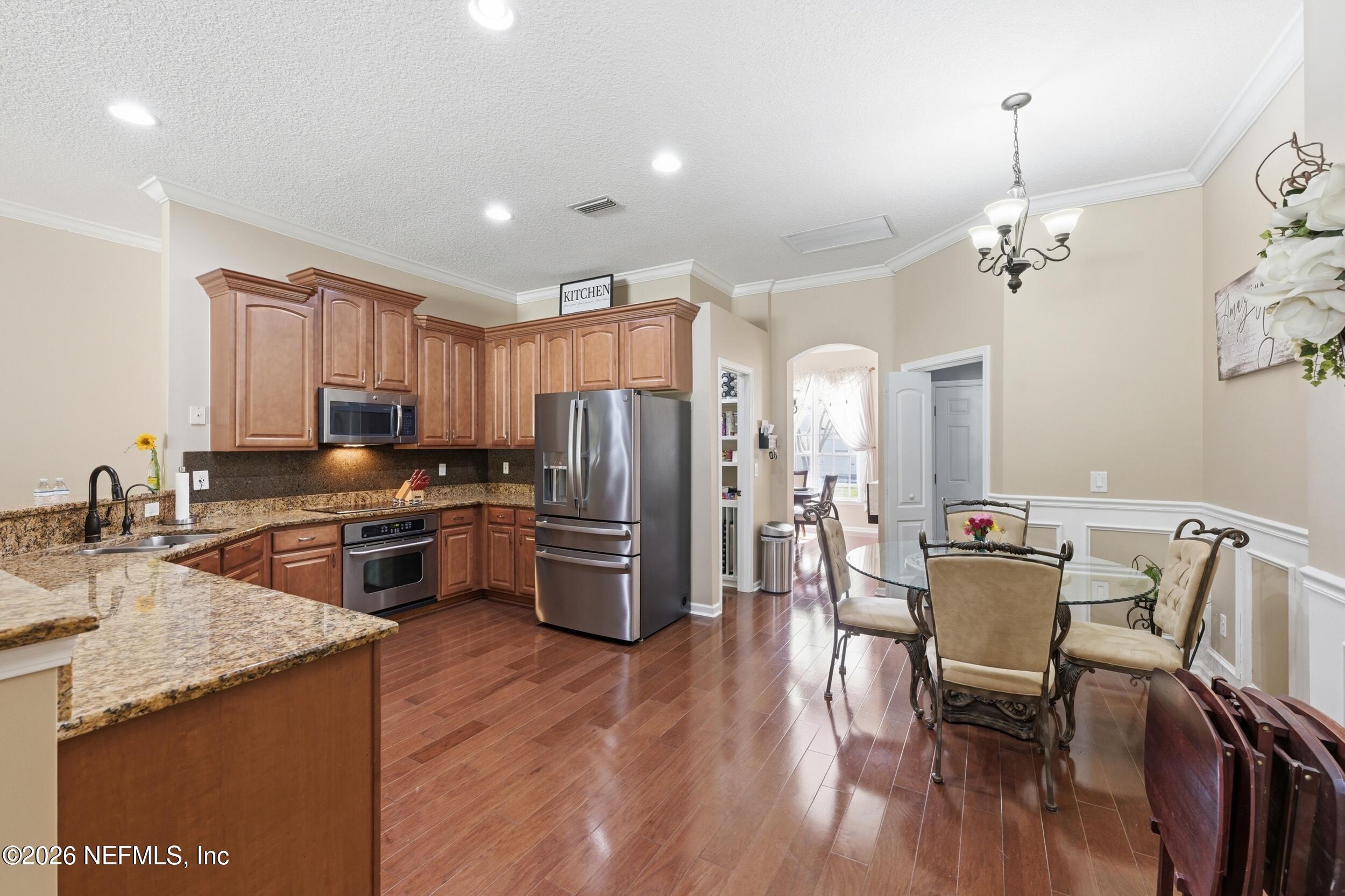 86178 Sand Hickory Trail Yulee, FL 32097 - Photo 9 of 23 a kitchen with stainless steel appliances granite countertop a refrigerator a stove top oven a sink dishwasher a dining table and chairs with wooden floor