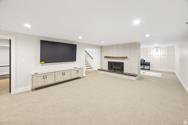 1774 Country Club Drive Logan, UT 84321 - Photo 19 of 28 Spacious room featuring a white brick fireplace with a wood mantel, an integrated wall-mounted media cabinet, and light-toned carpeting throughout