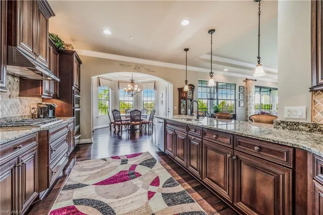 a kitchen with stainless steel appliances granite countertop a stove top oven a sink a dining table and chairs with wooden floor