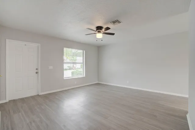 an empty room with wooden floor ceiling fan and windows