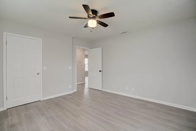 an empty room with wooden floor ceiling fan and window