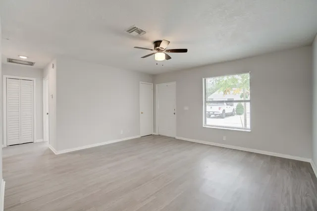 an empty room with wooden floor ceiling fan and windows