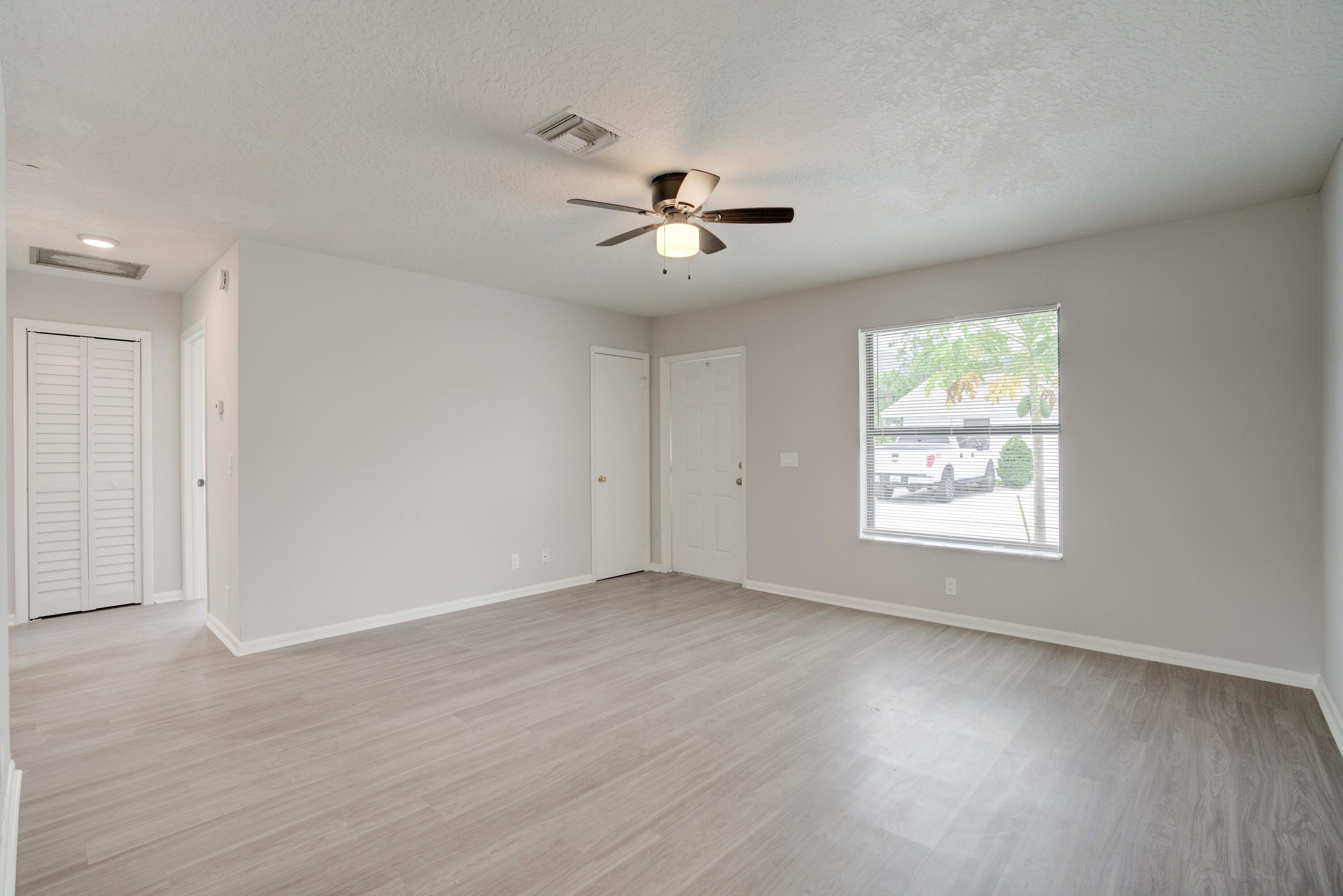 6567 Jupiter Gardens Boulevard, Unit 7 Jupiter, FL 33458 - Photo 5 of 20 an empty room with wooden floor ceiling fan and windows