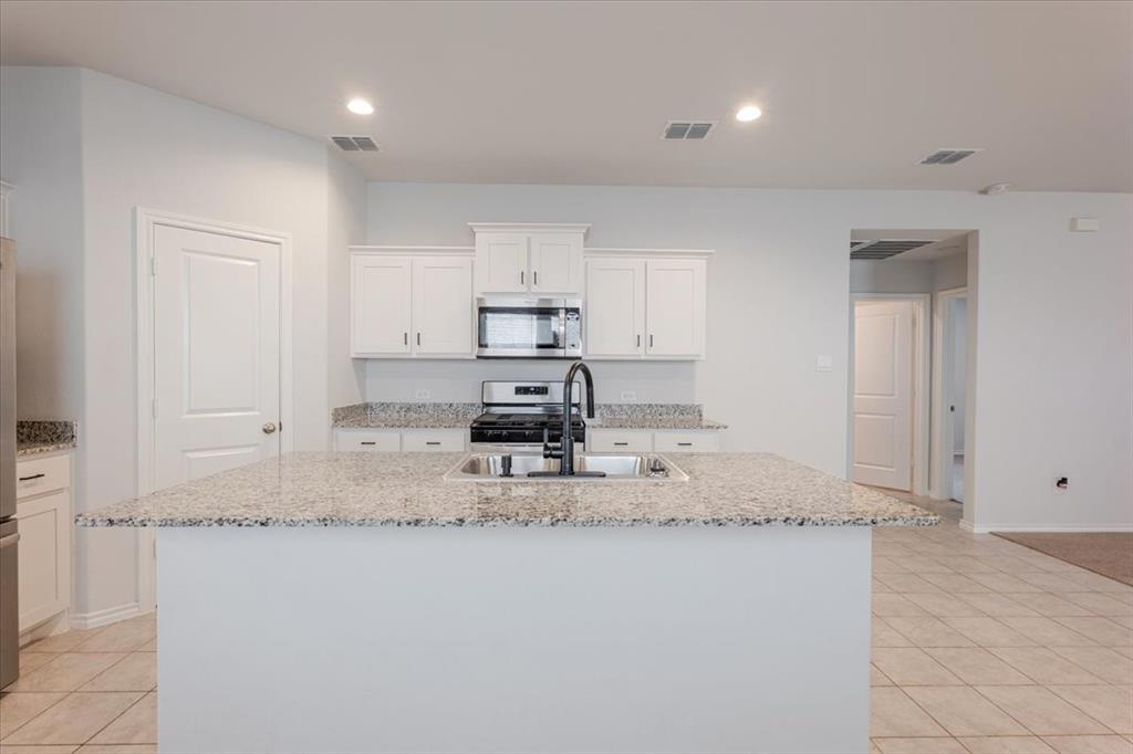 Kitchen with light tile patterned floors, recessed lighting, appliances with stainless steel finishes, an island with sink, and white cabinetry