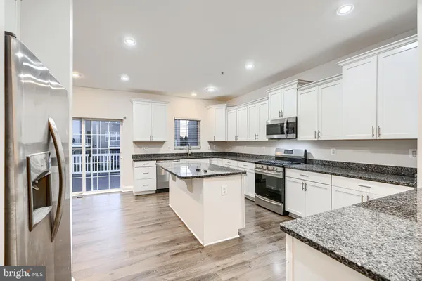 a kitchen with stainless steel appliances granite countertop a stove top oven a sink dishwasher and a refrigerator with wooden floor